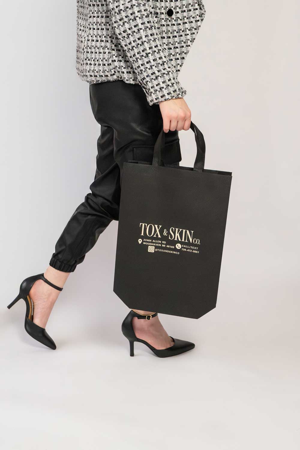 Person walking in heels carrying a Tox & Skin Co. branded shopping bag.